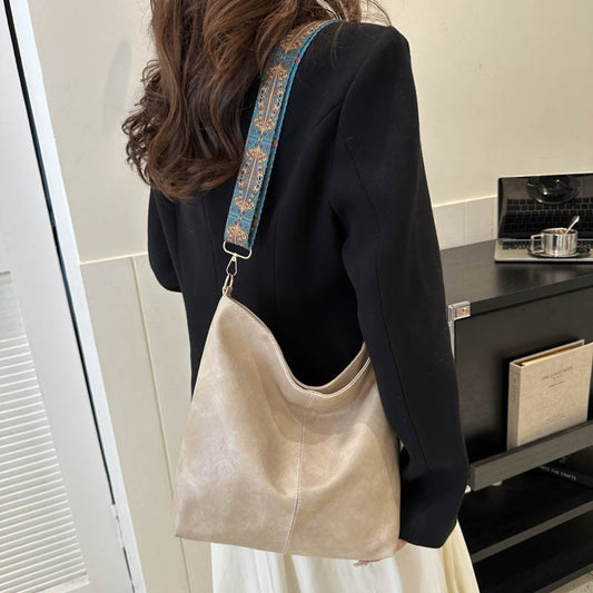Person wearing a beige shoulder bag with a decorative strap in an indoor setting.