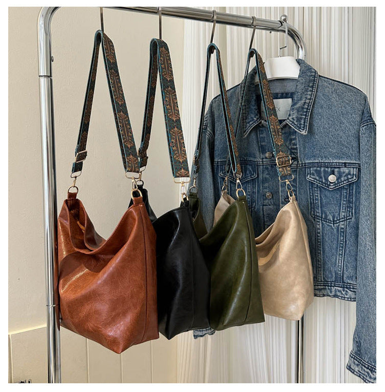 Four leather handbags in different colors hanging on a rack with a denim jacket.
