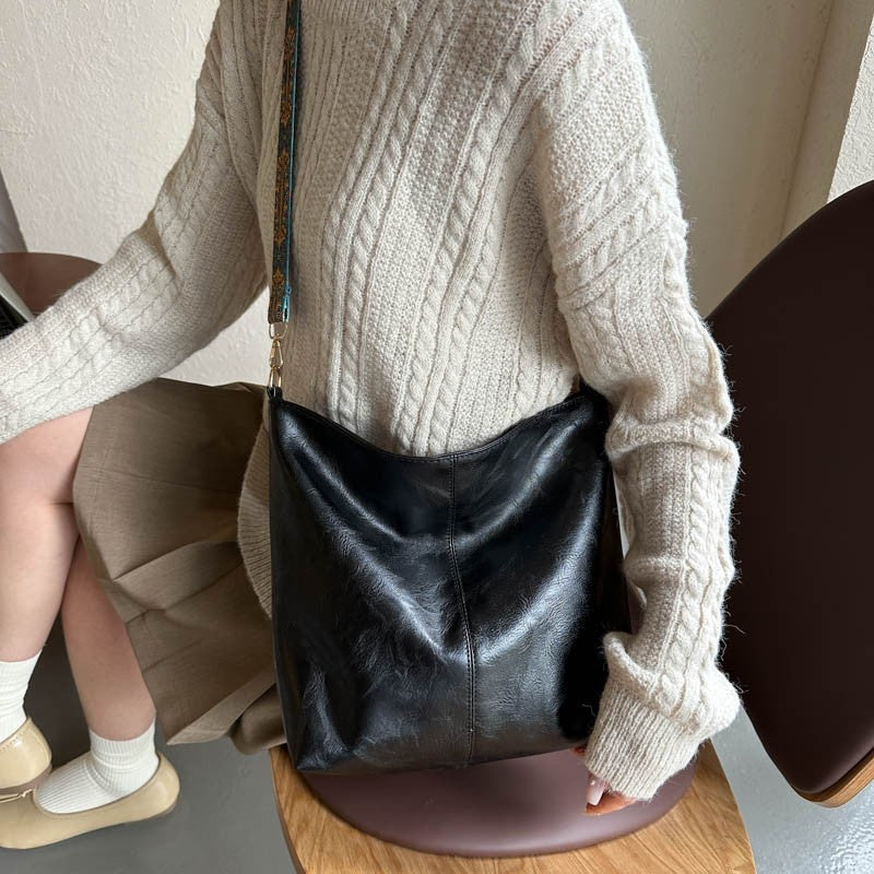 Person wearing a beige sweater and holding a black leather bag.