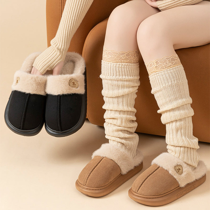 Pair of black and brown slippers held by a person wearing beige leg warmers.