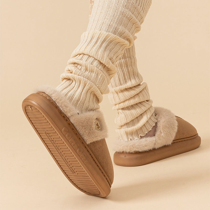 Beige slippers with fluffy fur trim worn with cream ribbed socks on a beige background