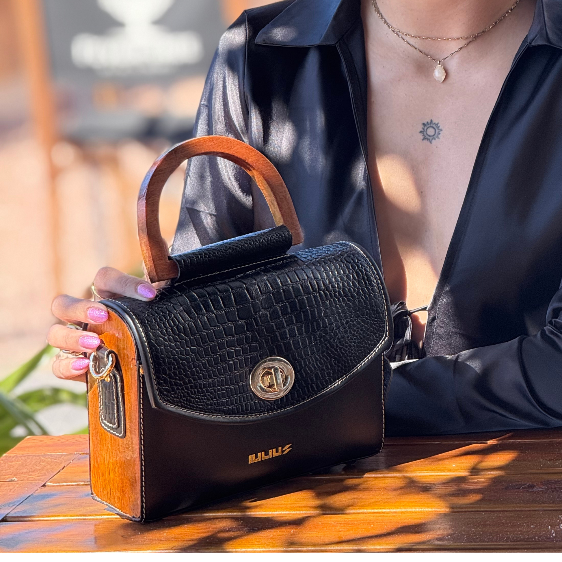Person holding a black handbag with wooden handle on a table outdoors