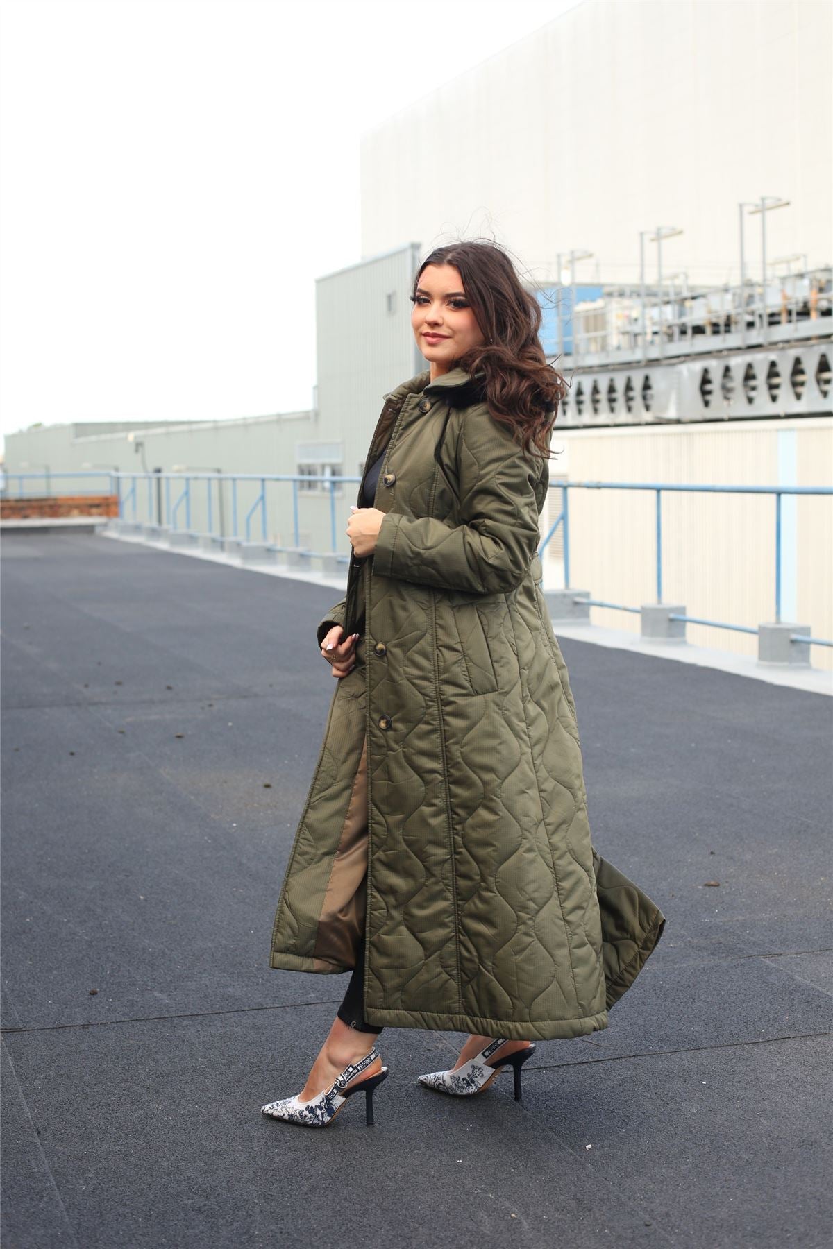 Woman wearing a long green coat on a rooftop with buildings in the background