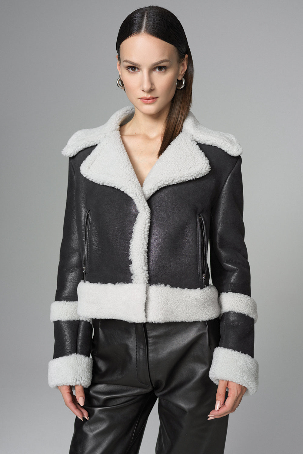 Black leather jacket with white fur trim worn by a model on a gray background