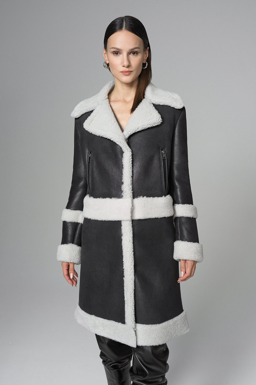 Woman wearing a black leather coat with white fur trim on a gray background