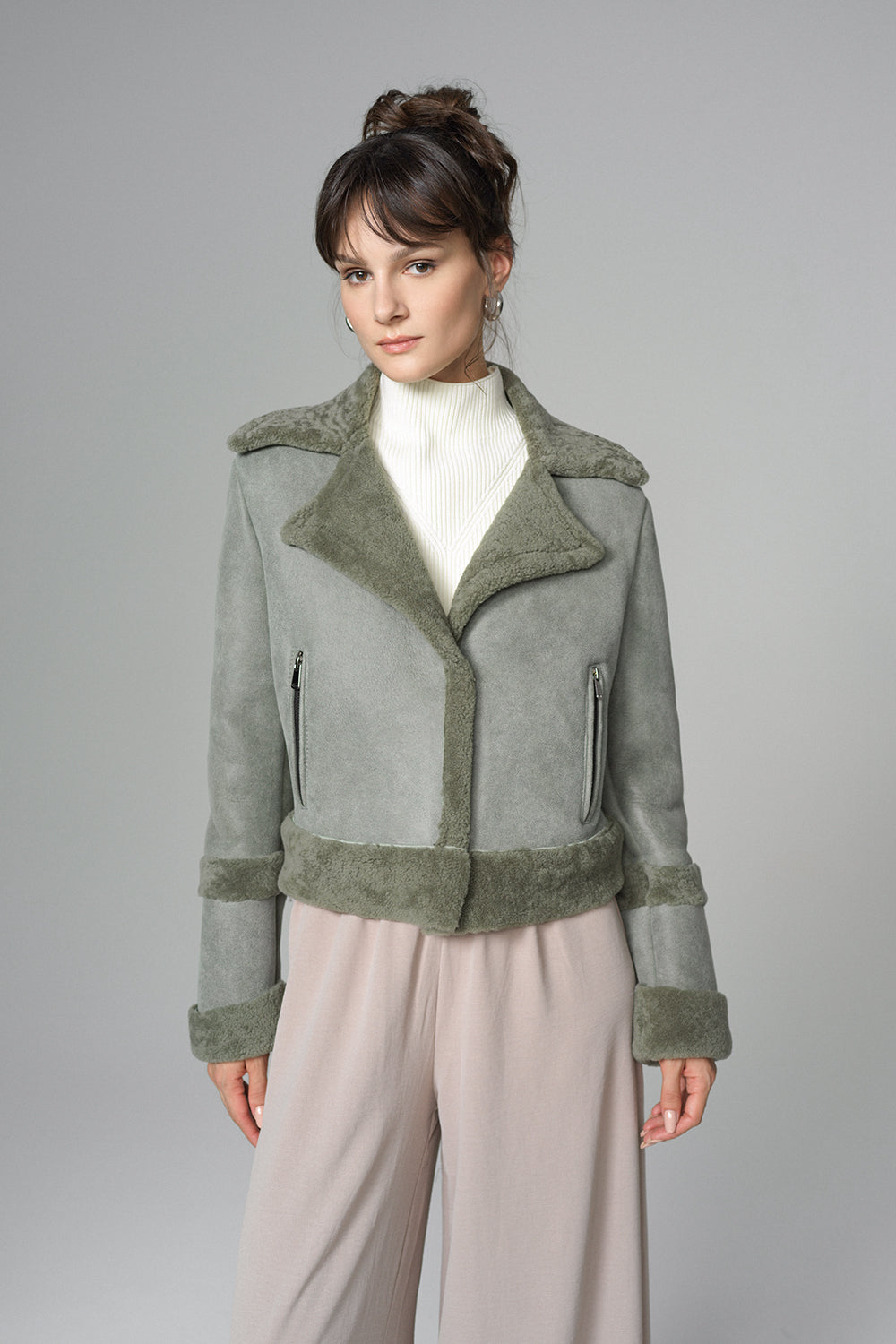Woman wearing a gray jacket with green trim on a gray background
