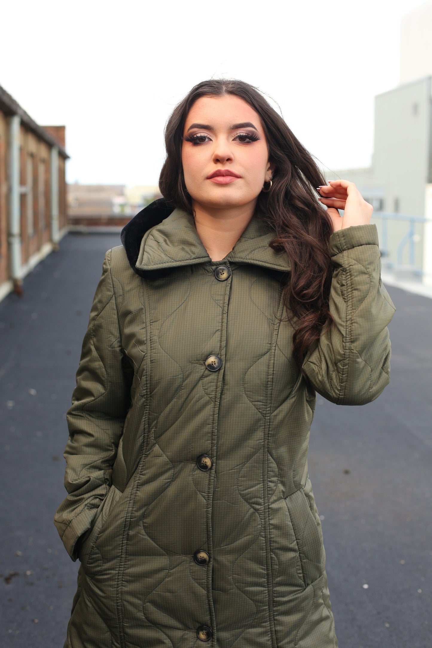 Woman wearing a green coat standing on an urban rooftop.
