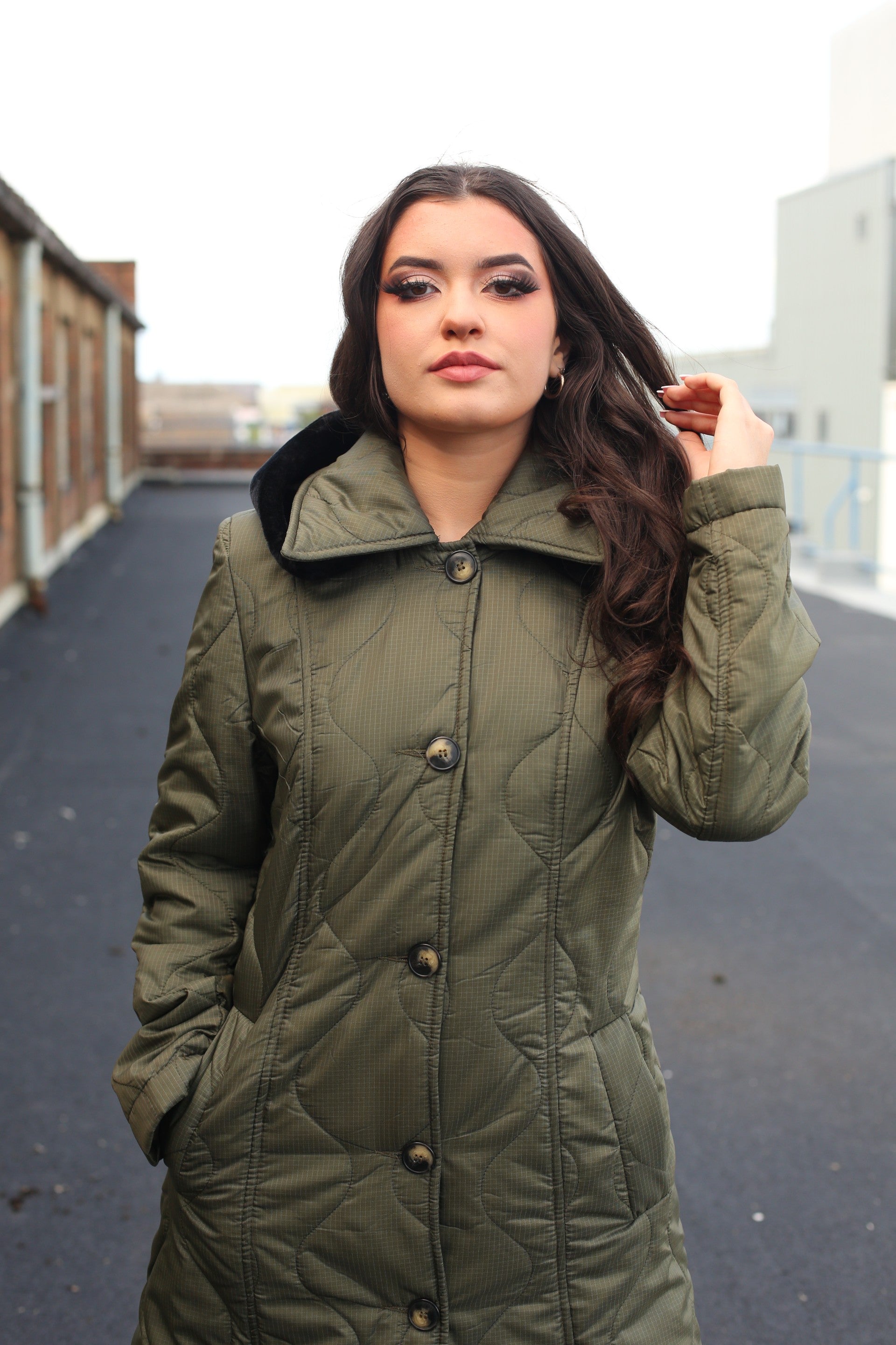 Woman wearing a green coat standing on an urban rooftop.