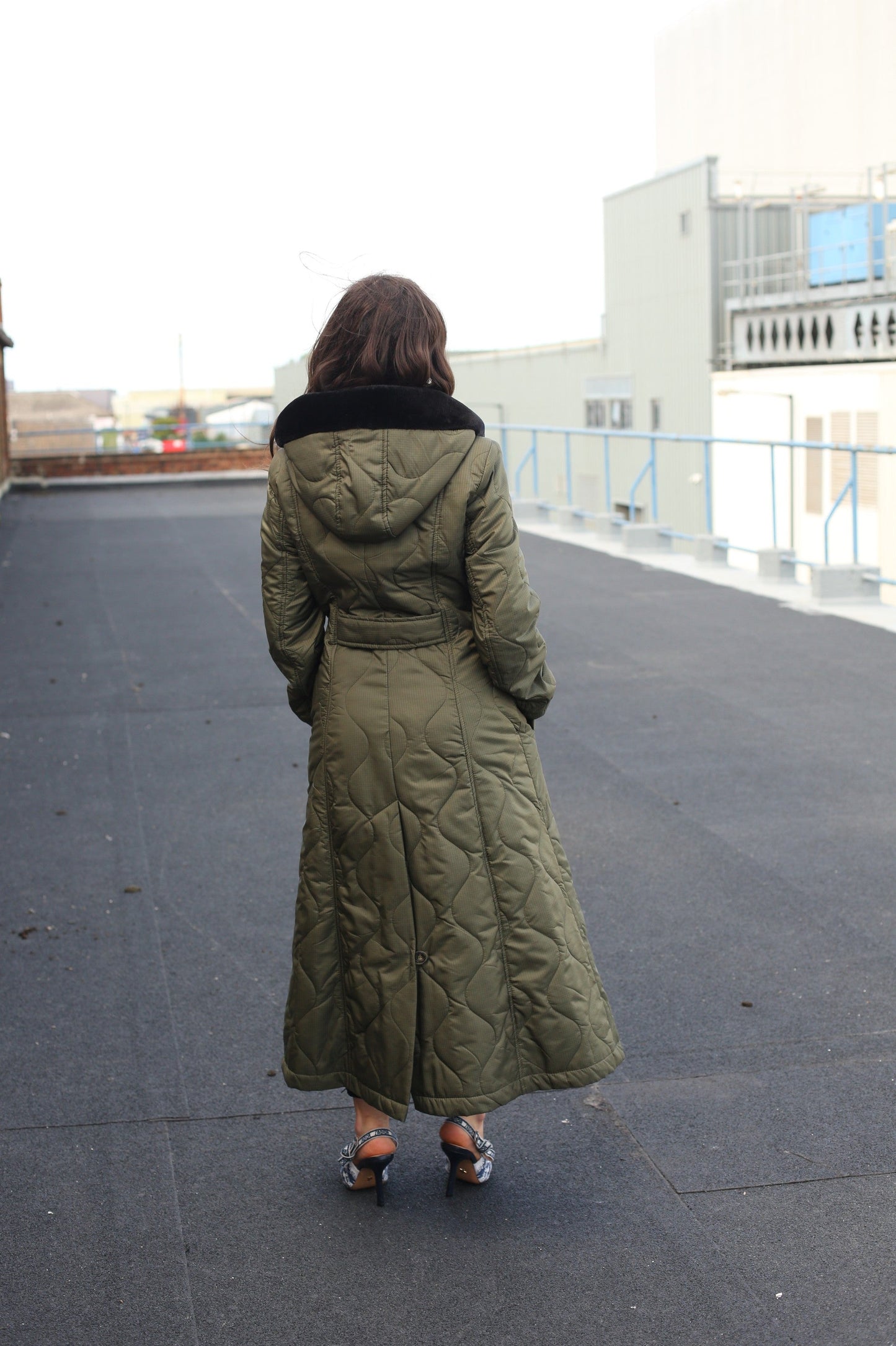 Person wearing a long green coat on a rooftop with buildings in the background