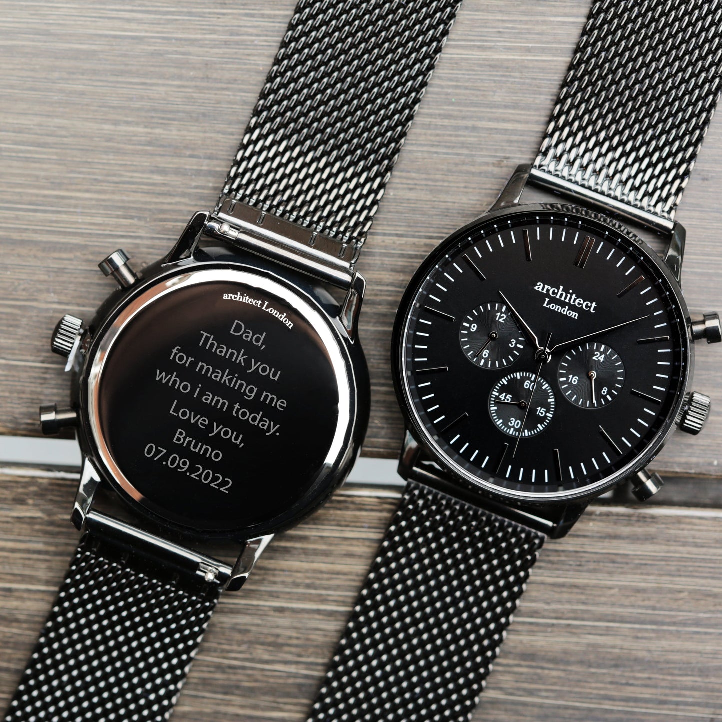 Two black wristwatches with mesh bands on a wooden surface