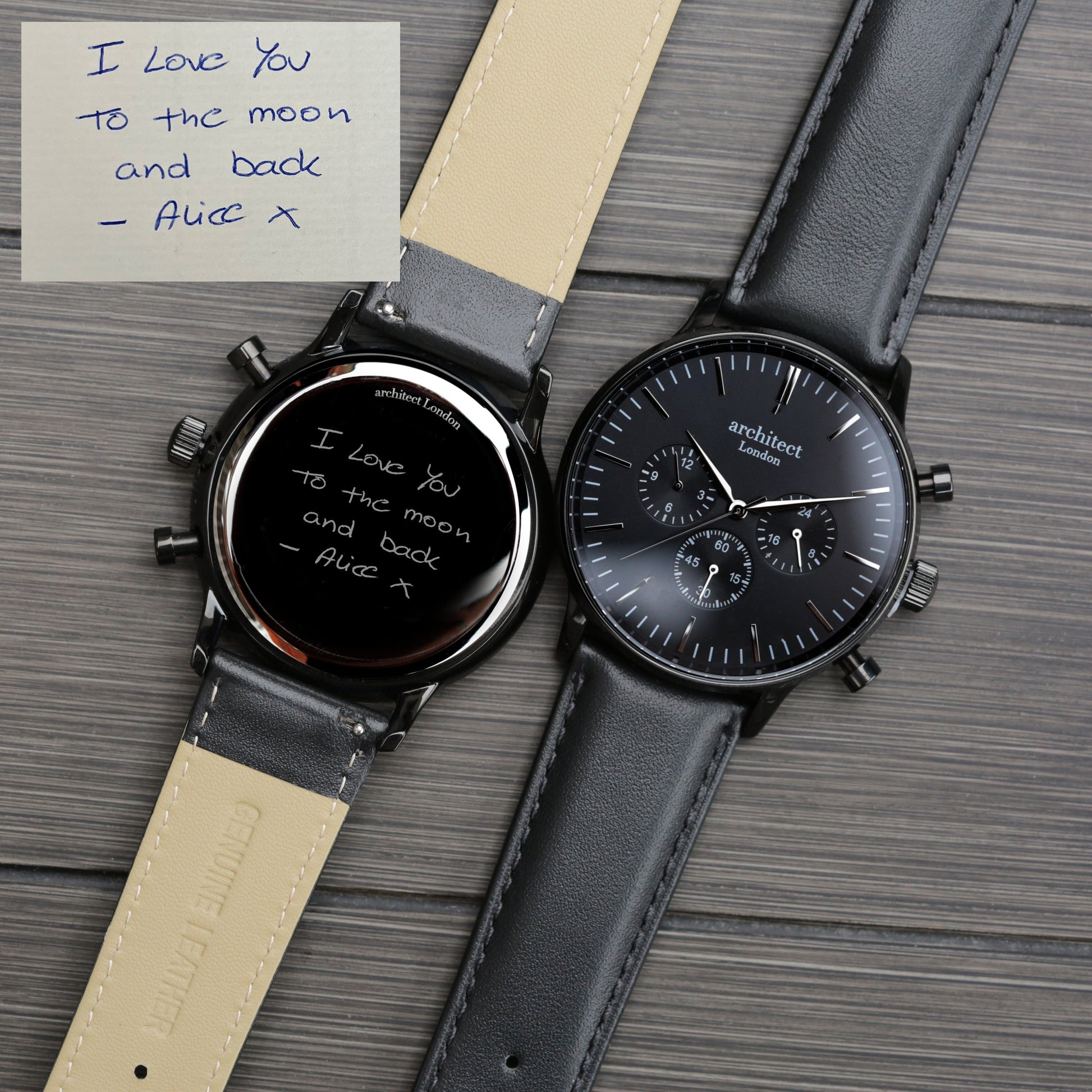 Two watches with black faces and leather straps on a wooden surface, one with a handwritten note.