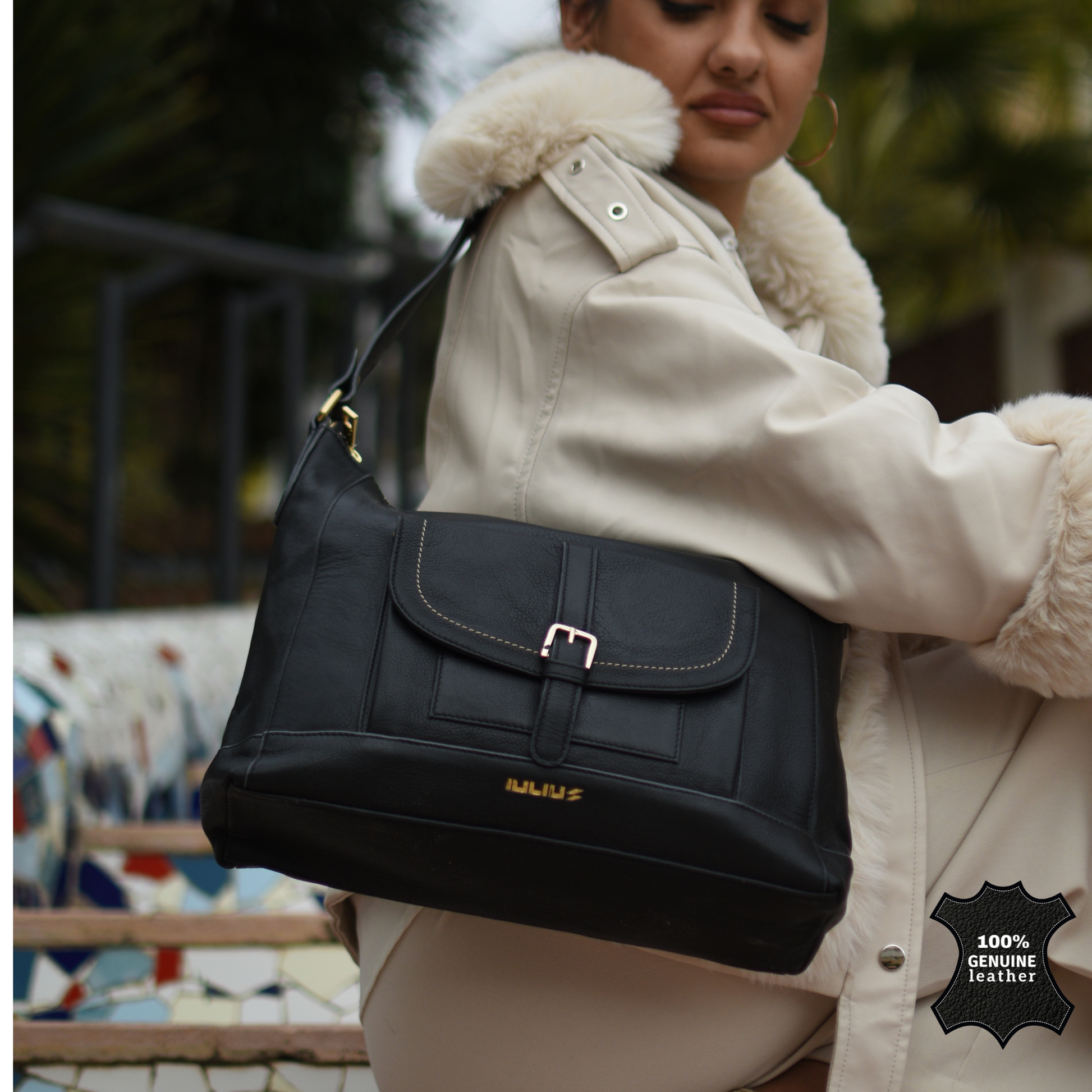 Person wearing a cream coat with fur collar holding a black handbag, with a visible brand logo.