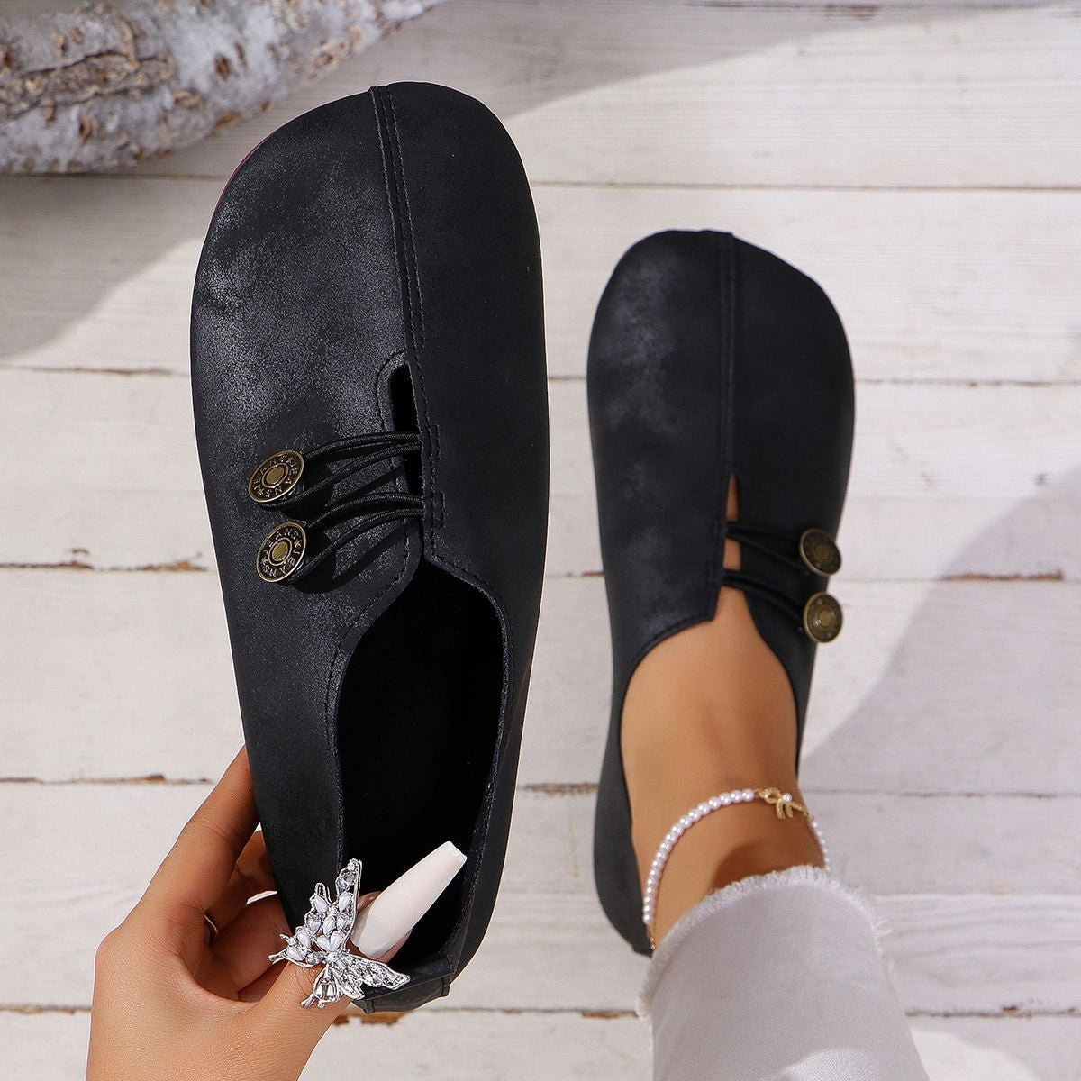 Black loafers with gold buttons worn indoors on a wooden floor.