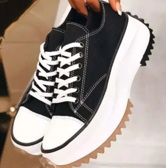 Black and white sneakers with a thick sole held by a hand.