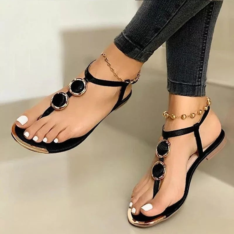 Black sandals with gold accents worn by a person on a neutral background