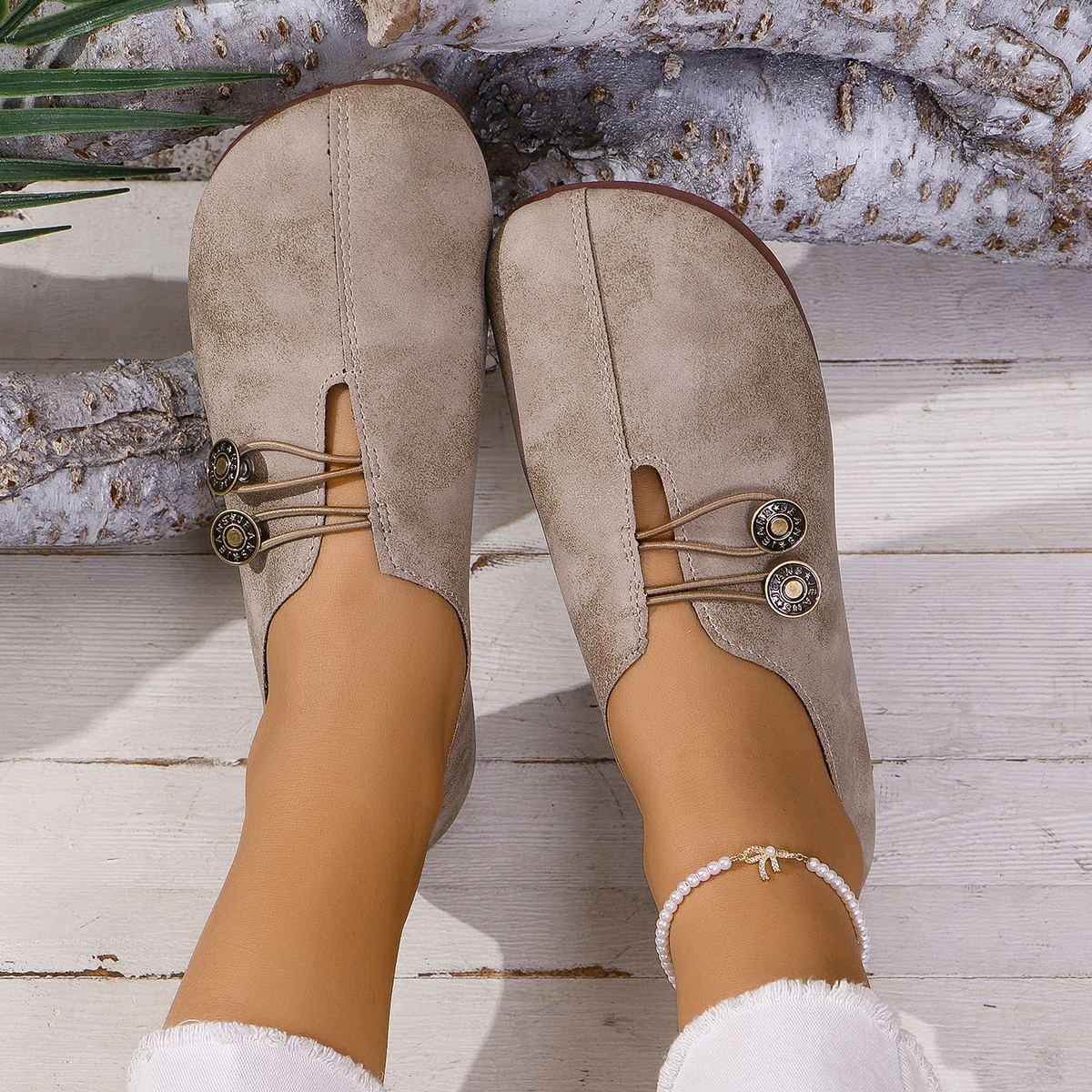Beige suede shoes with decorative laces on a wooden floor.
