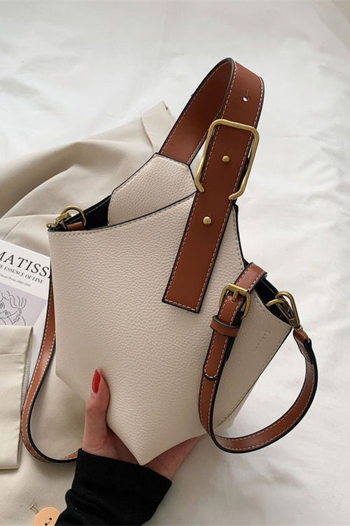 White handbag with brown leather straps held by a hand on a light background