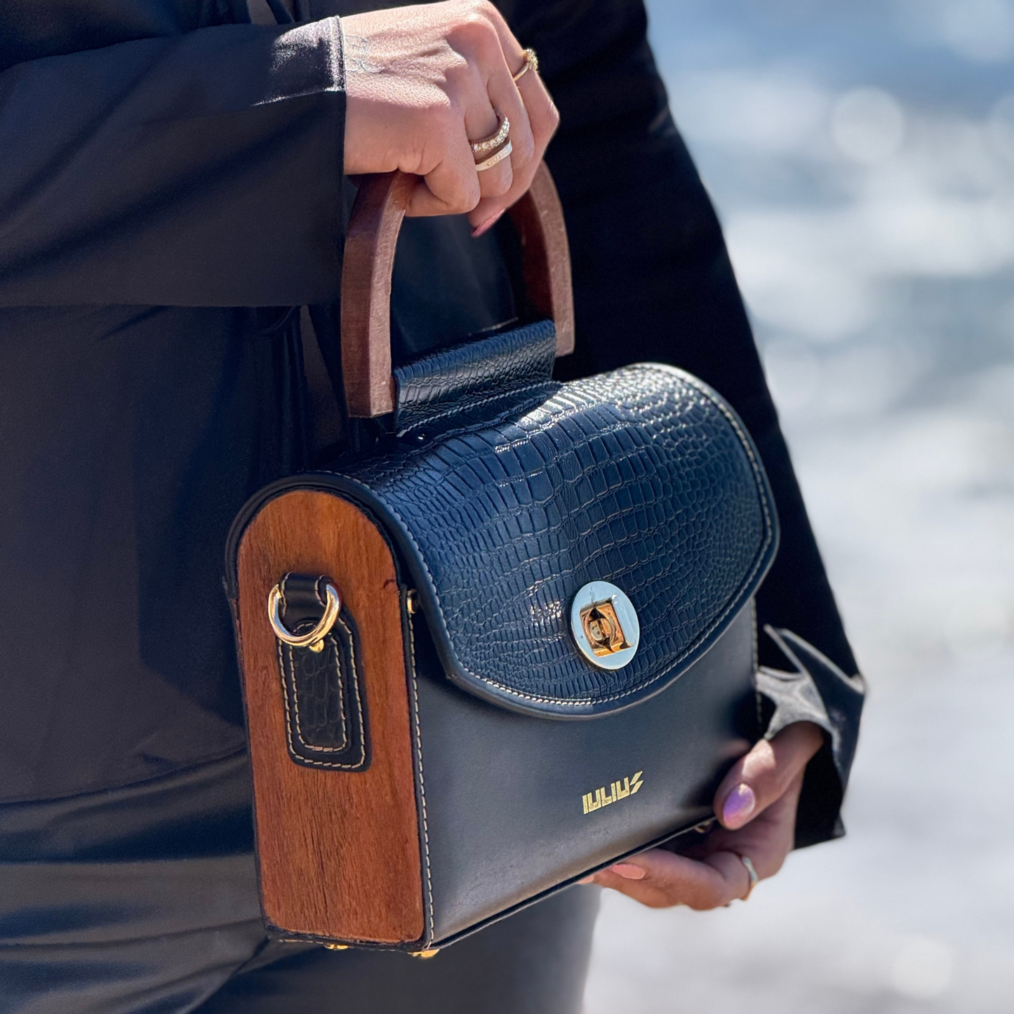Handbag with wooden accents held by a person against a blurred natural background