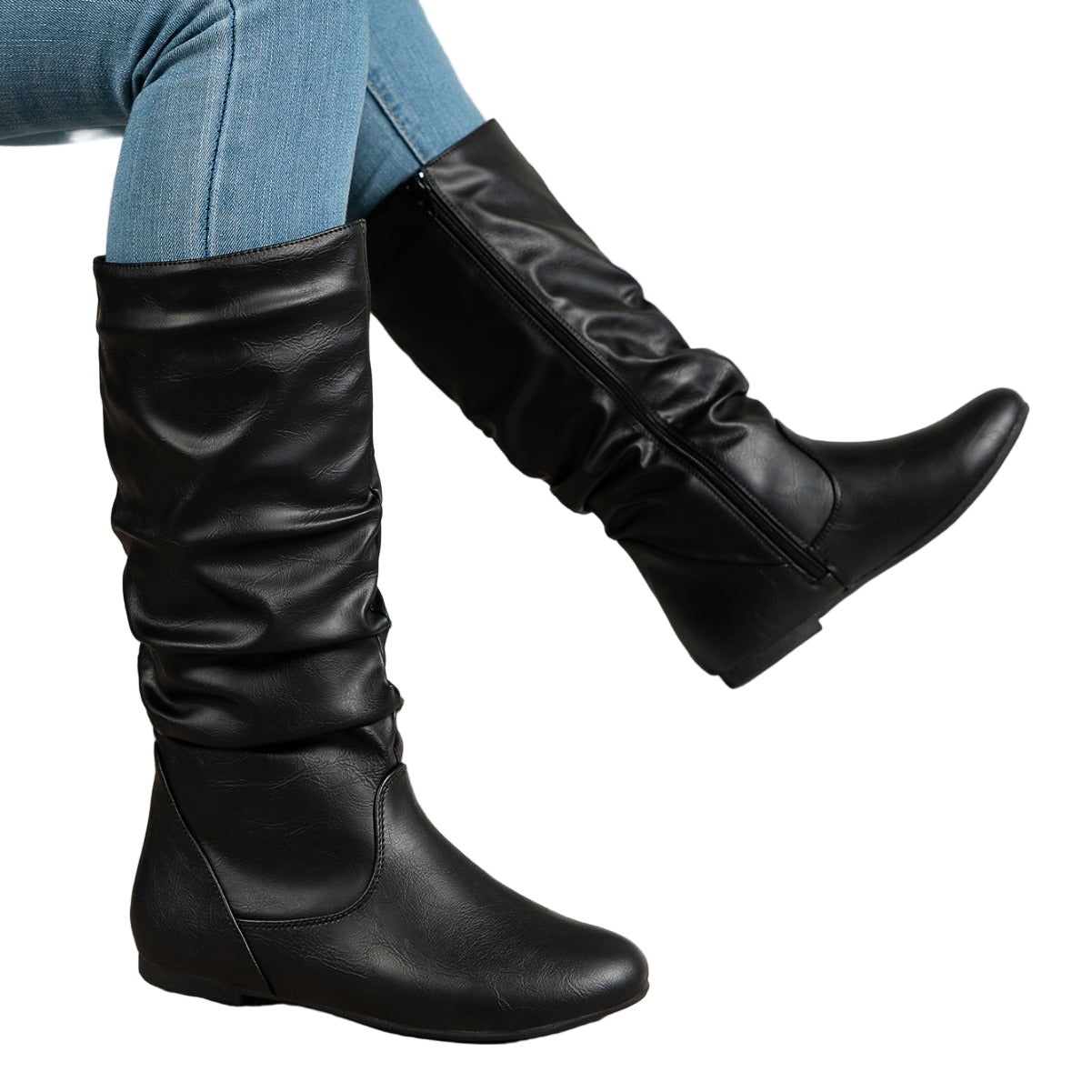 Black knee-high boots worn with blue jeans on a white background