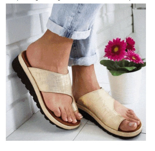 Person wearing beige sandals with a white background and a plant in the corner