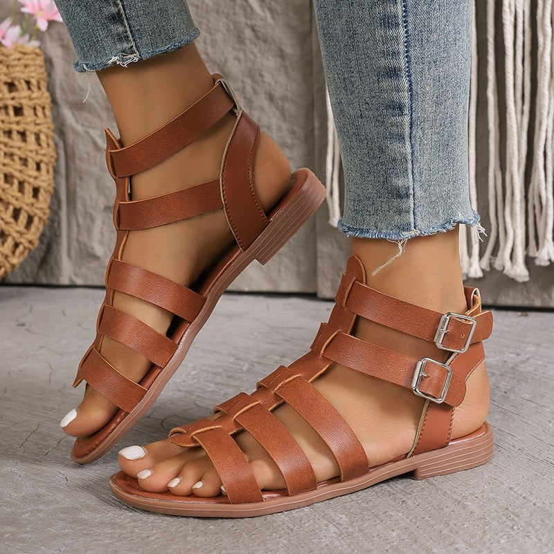 Brown strappy sandals worn with jeans on a neutral background