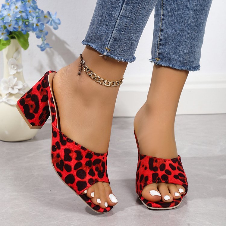 Red leopard print high-heeled shoes worn with blue jeans on a light gray surface.