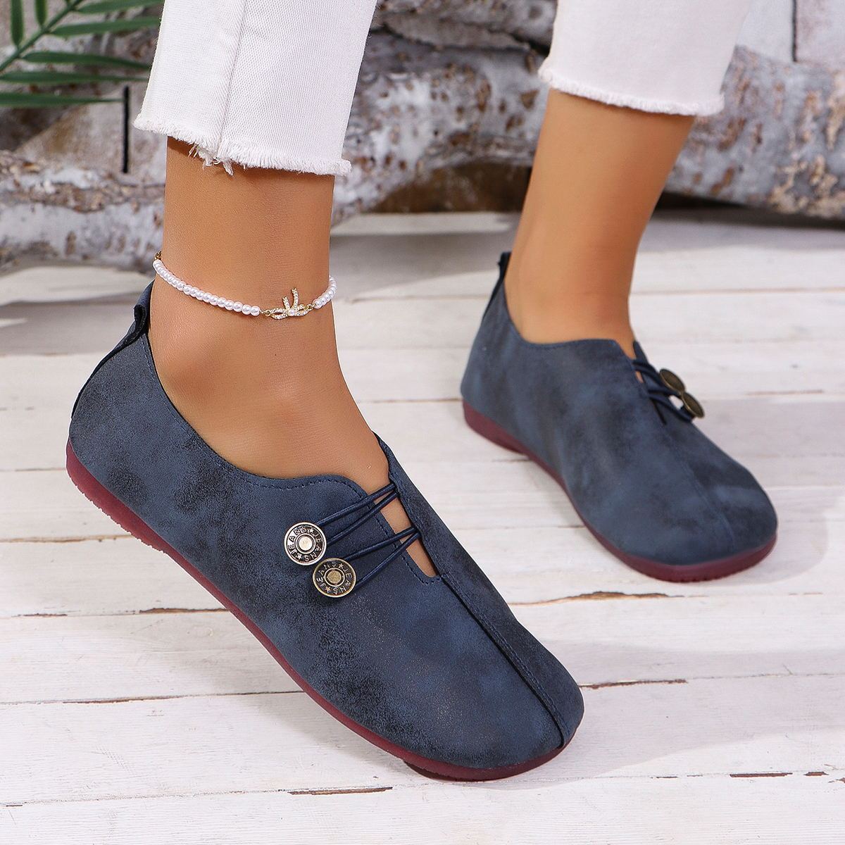 Blue suede shoes with buttons worn by a person on a wooden floor.