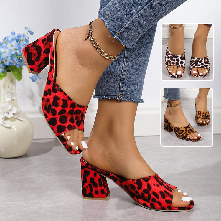 Red and black leopard print high-heeled shoes worn with denim jeans, on a light gray floor.
