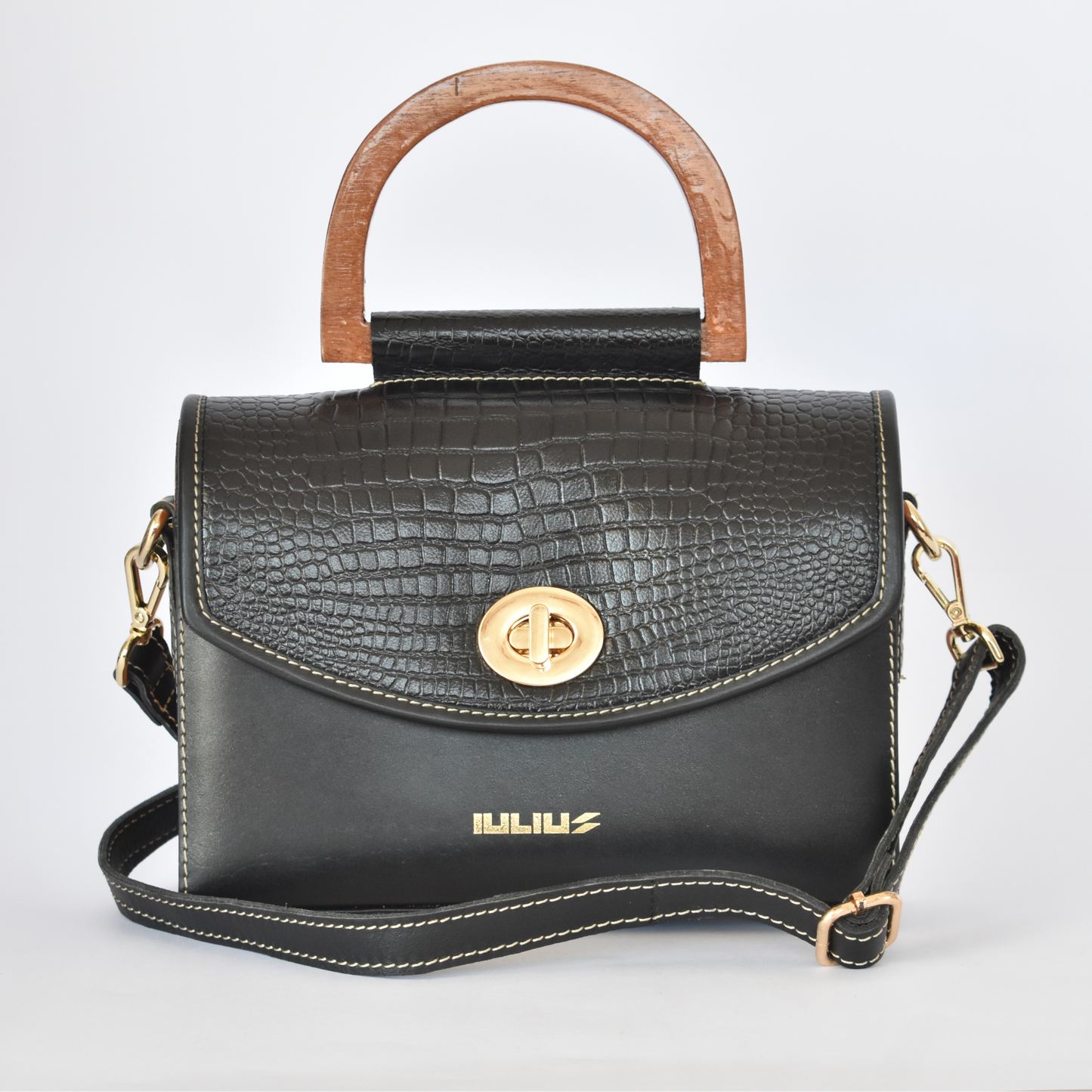Black handbag with wooden handle and gold accents on a light gray background