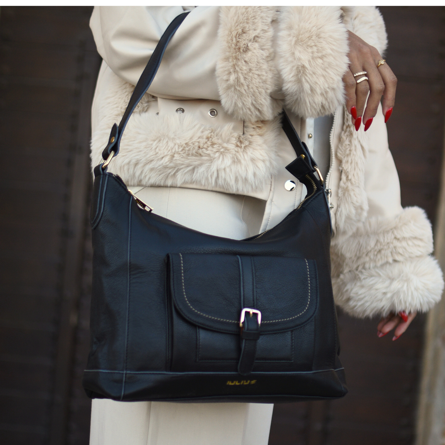Black handbag held by a person wearing a white coat with fur trim.