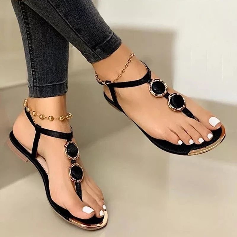 Black sandals with gold accents worn by a person on a neutral background