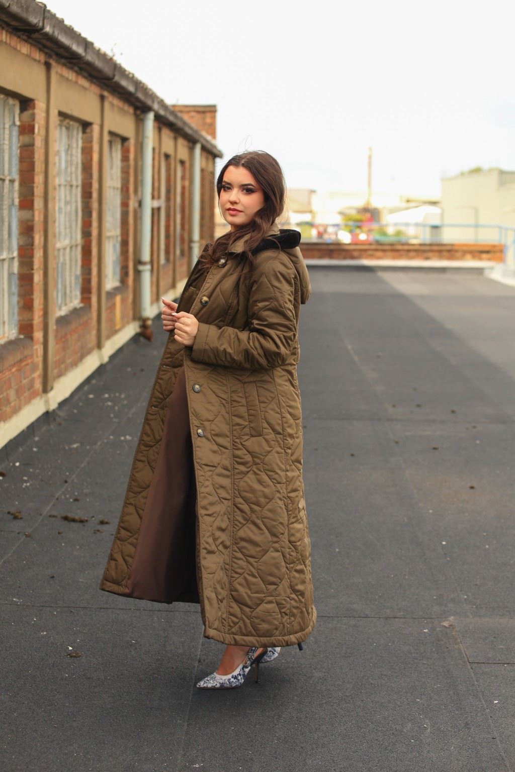 Woman wearing a long quilted brown coat on a rooftop.