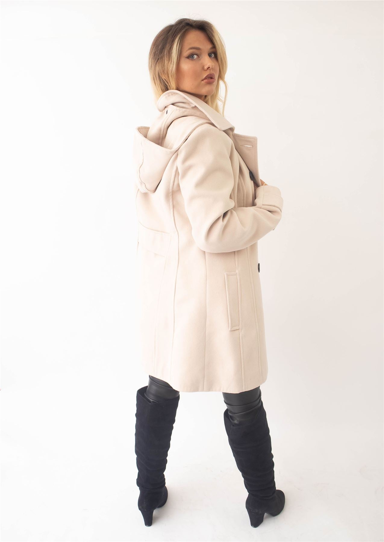 Woman wearing a beige coat and black knee-high boots on a white background