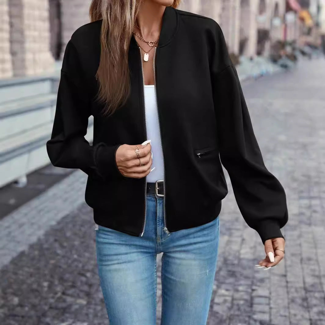 Person wearing a black bomber jacket and blue jeans on a street.
