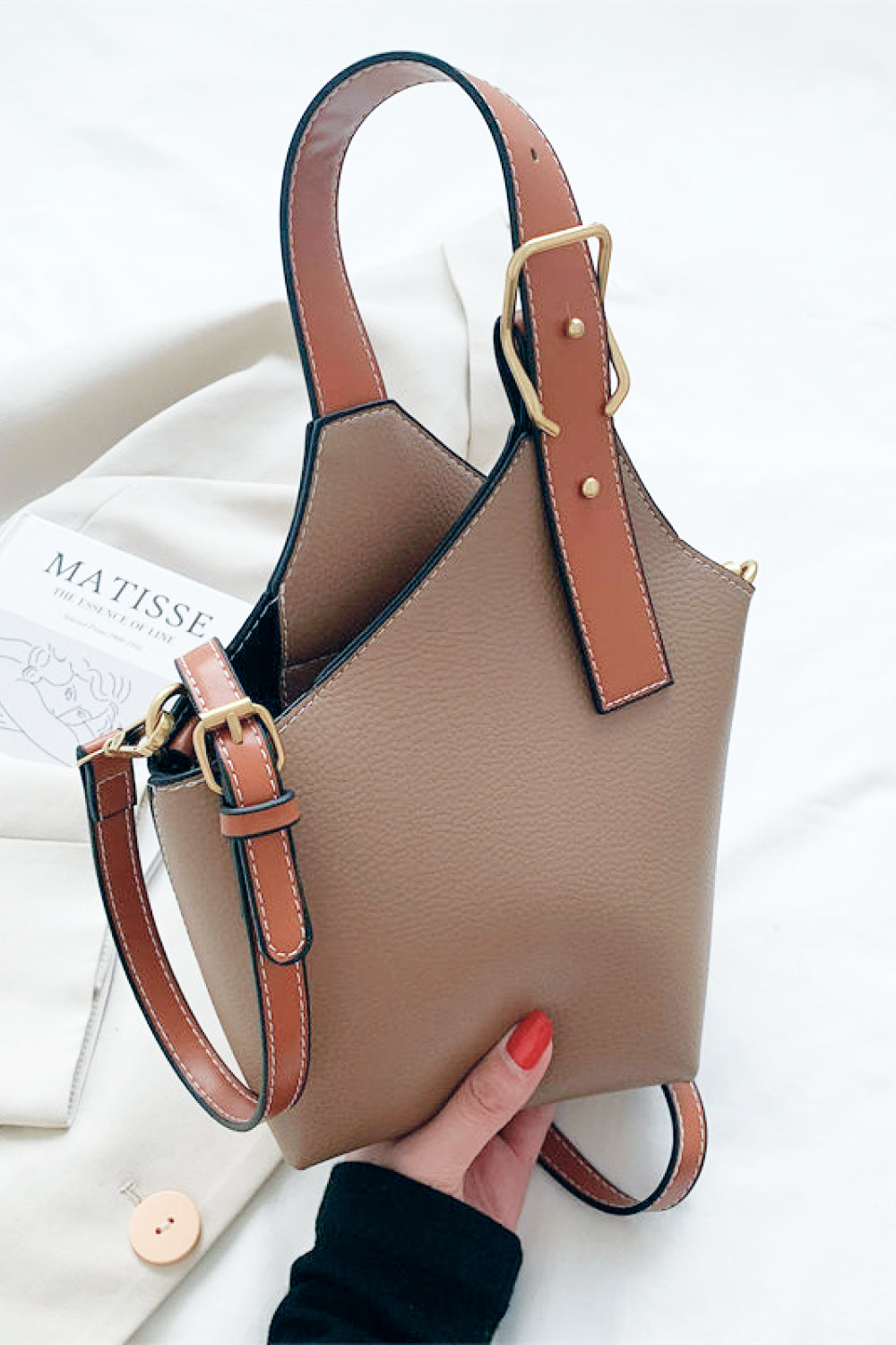 Beige handbag with brown straps held by a hand on a white background