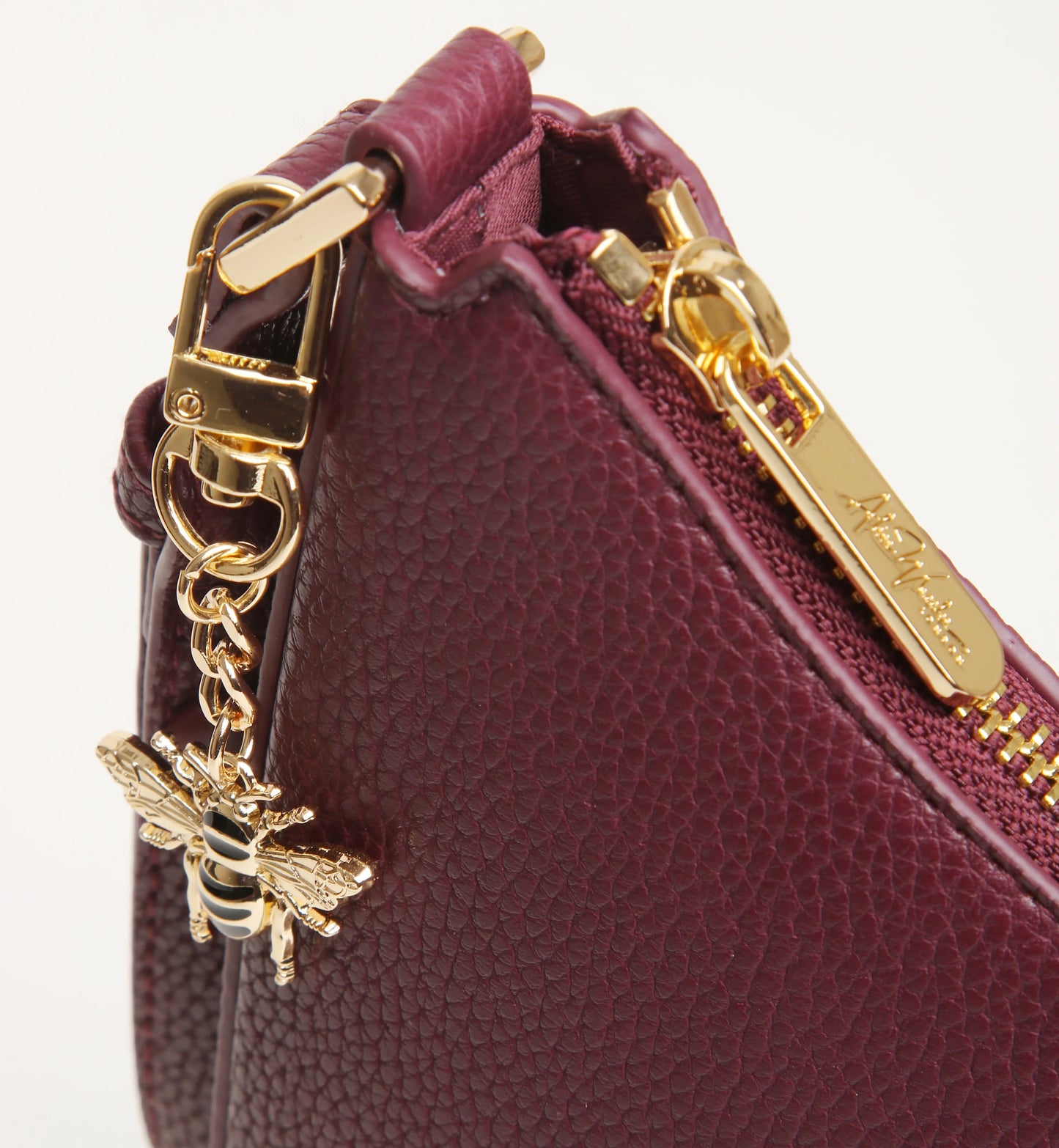 Close-up of a burgundy handbag with gold hardware and a bee charm on a white background