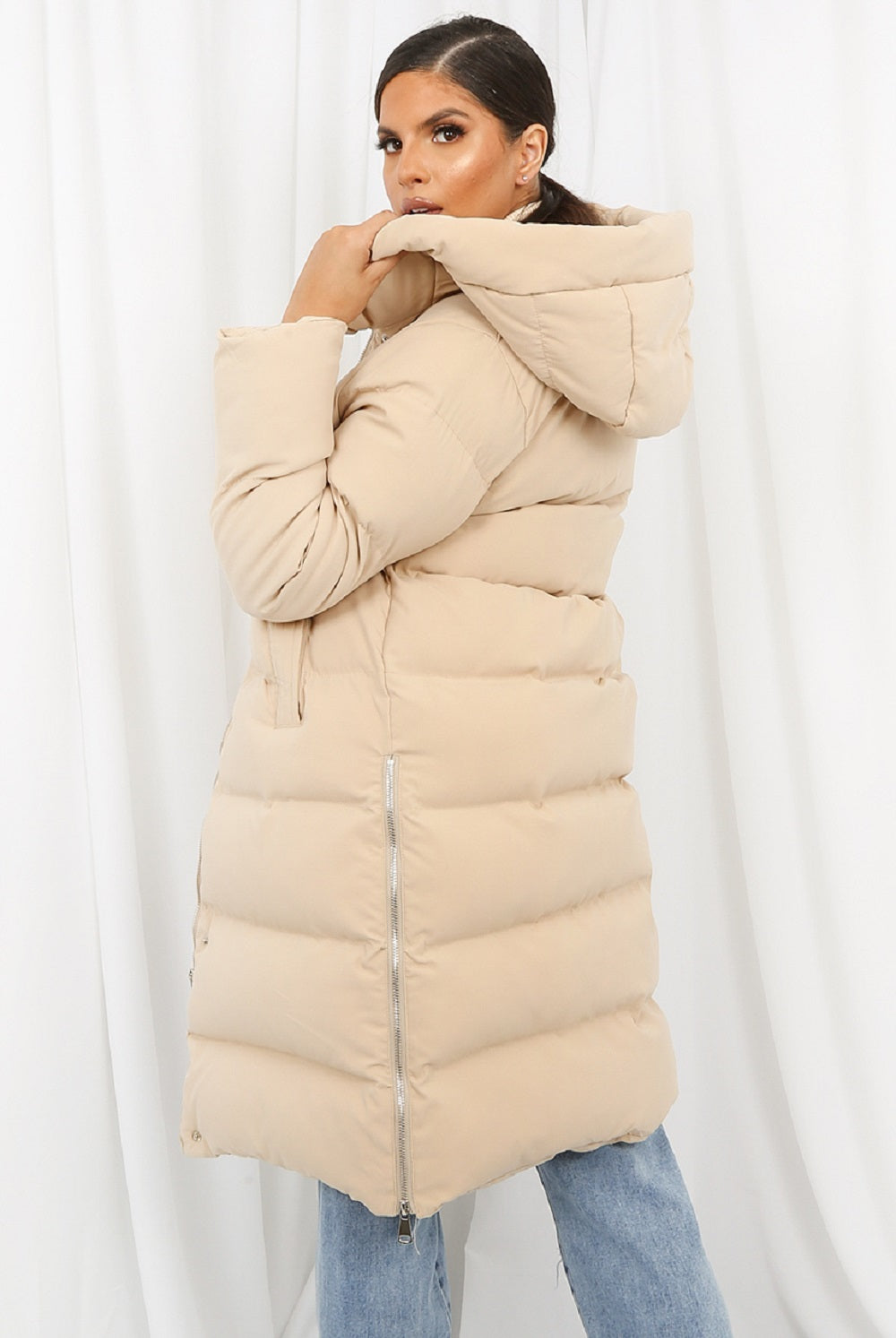 Woman wearing a beige puffer jacket against a white background