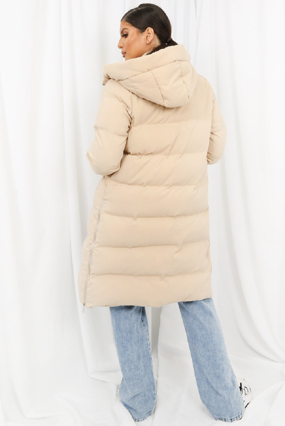 Person wearing a beige puffer coat and blue jeans on a white background