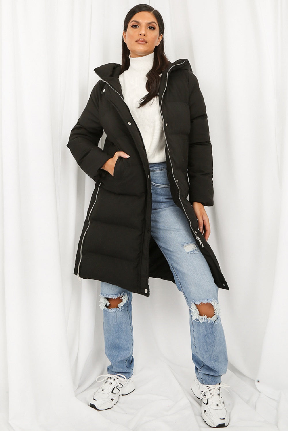 Person wearing a black puffer coat, white turtleneck, and ripped jeans on a white background