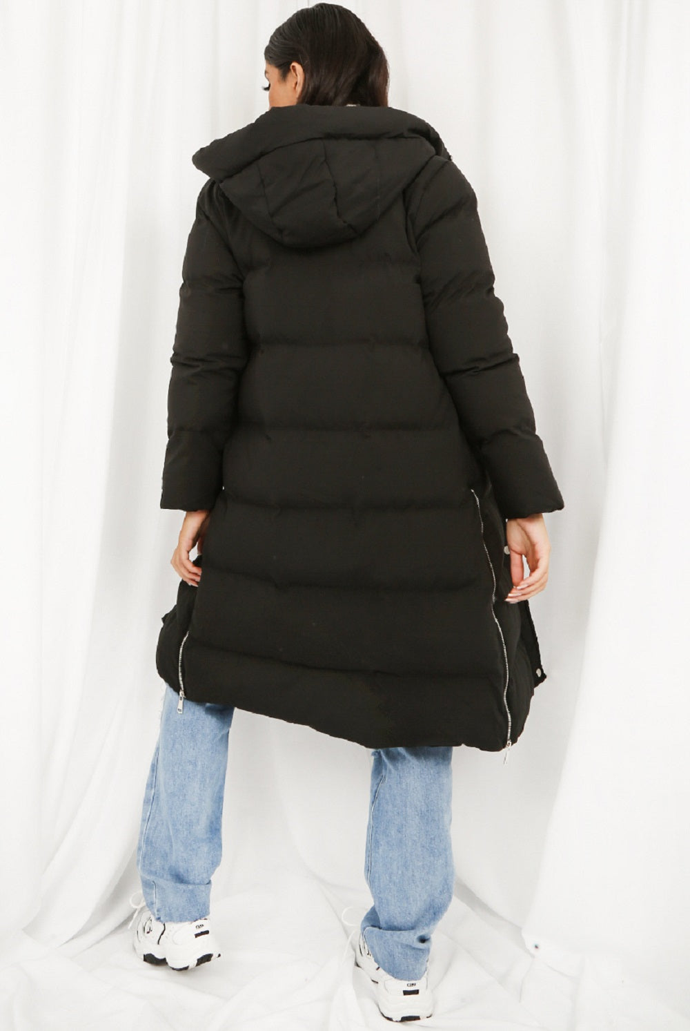 Person wearing a long black puffer coat on a white background