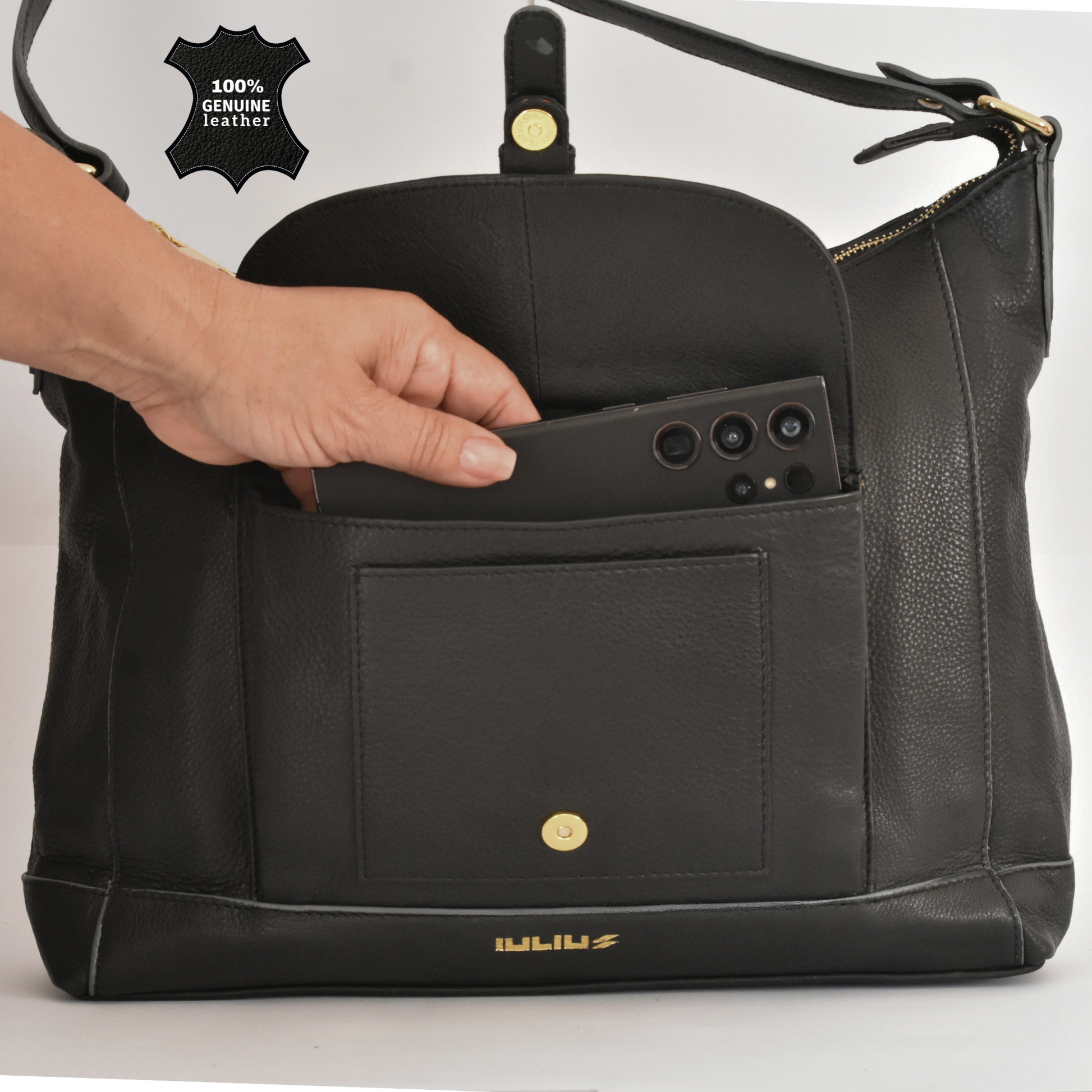 Black leather handbag with a phone case being placed inside, on a white background.