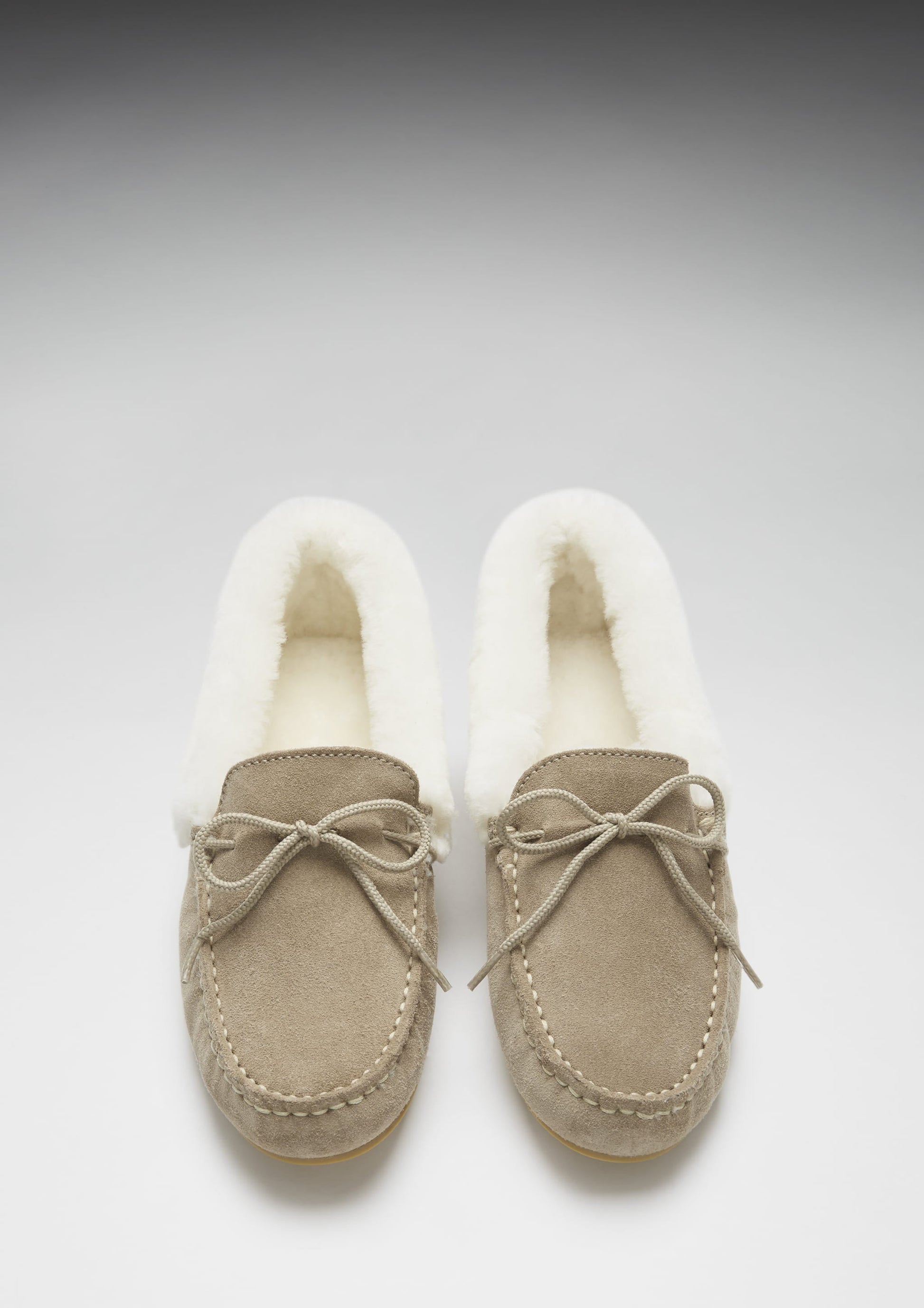 Pair of beige moccasin slippers with white fur lining on a light gray background
