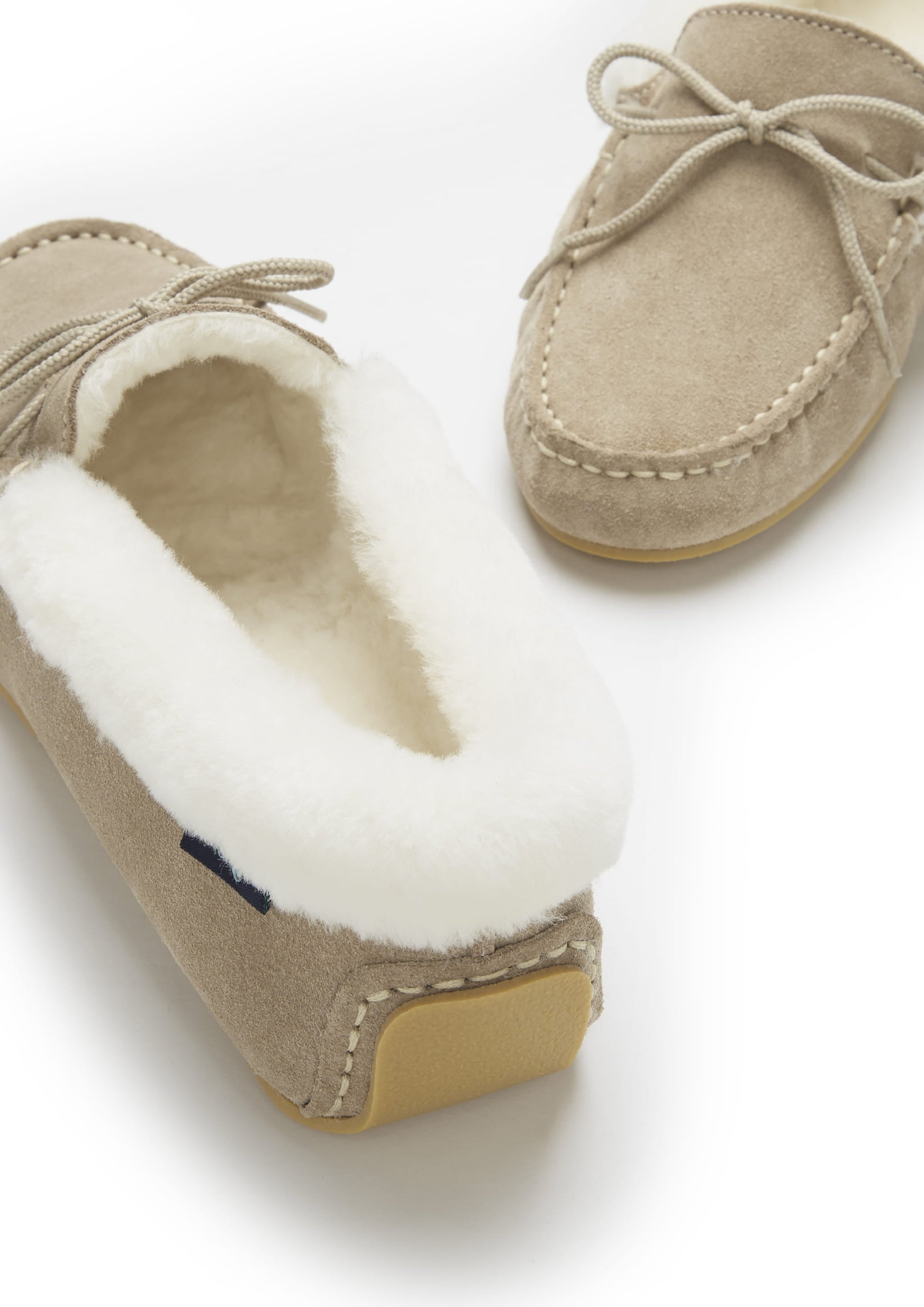 Pair of beige moccasin slippers with white fur lining on a light background