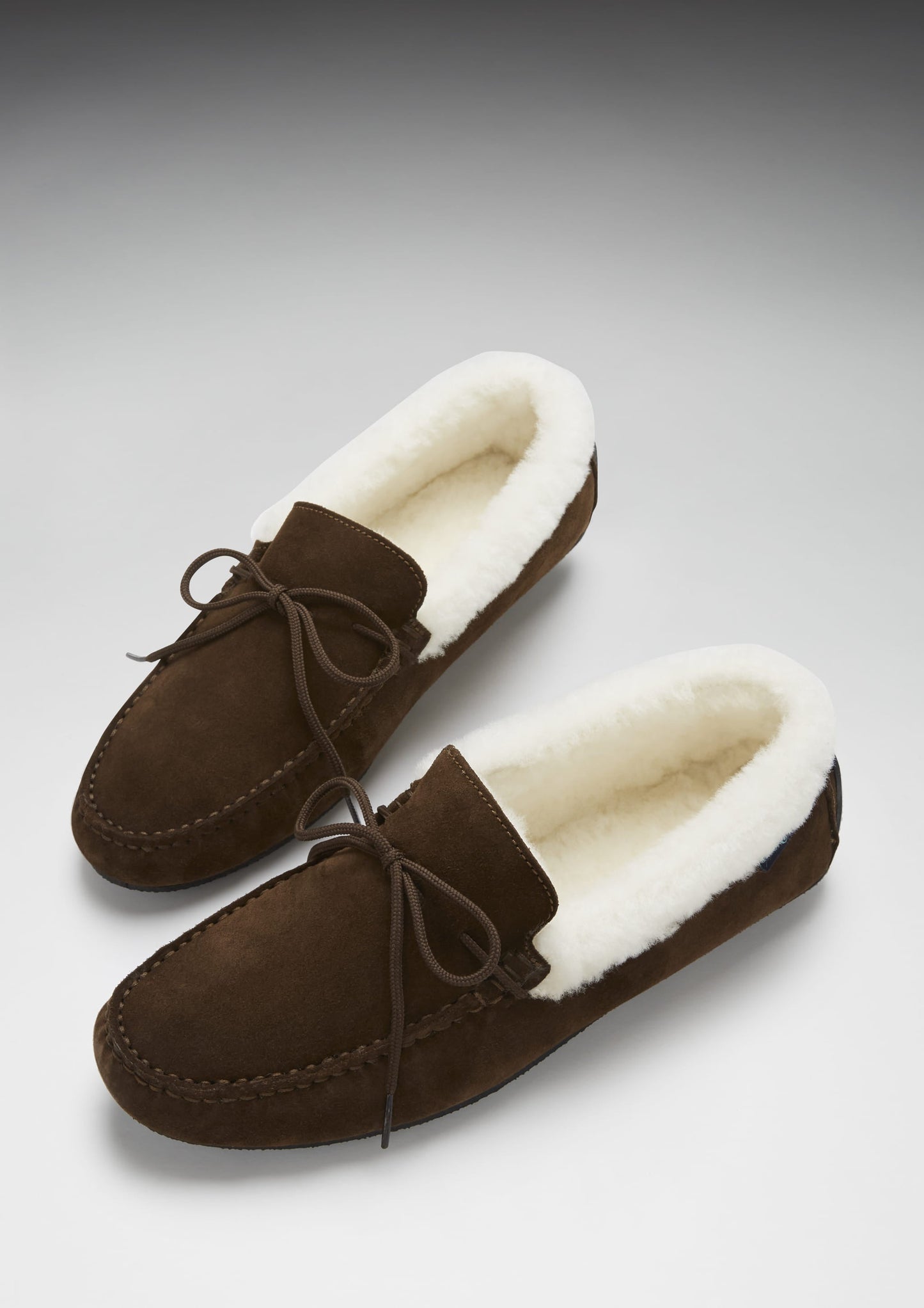 Brown suede slippers with white fur lining on a gray background