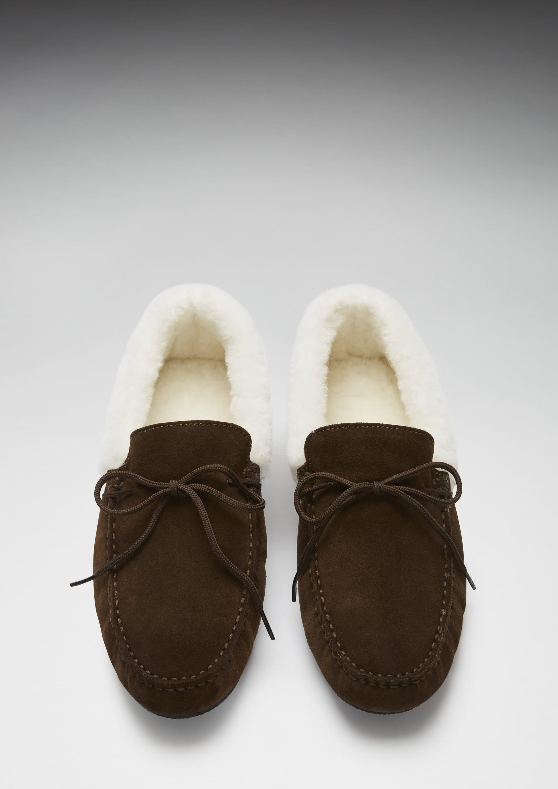 Pair of brown moccasin slippers with white fur lining on a light gray background