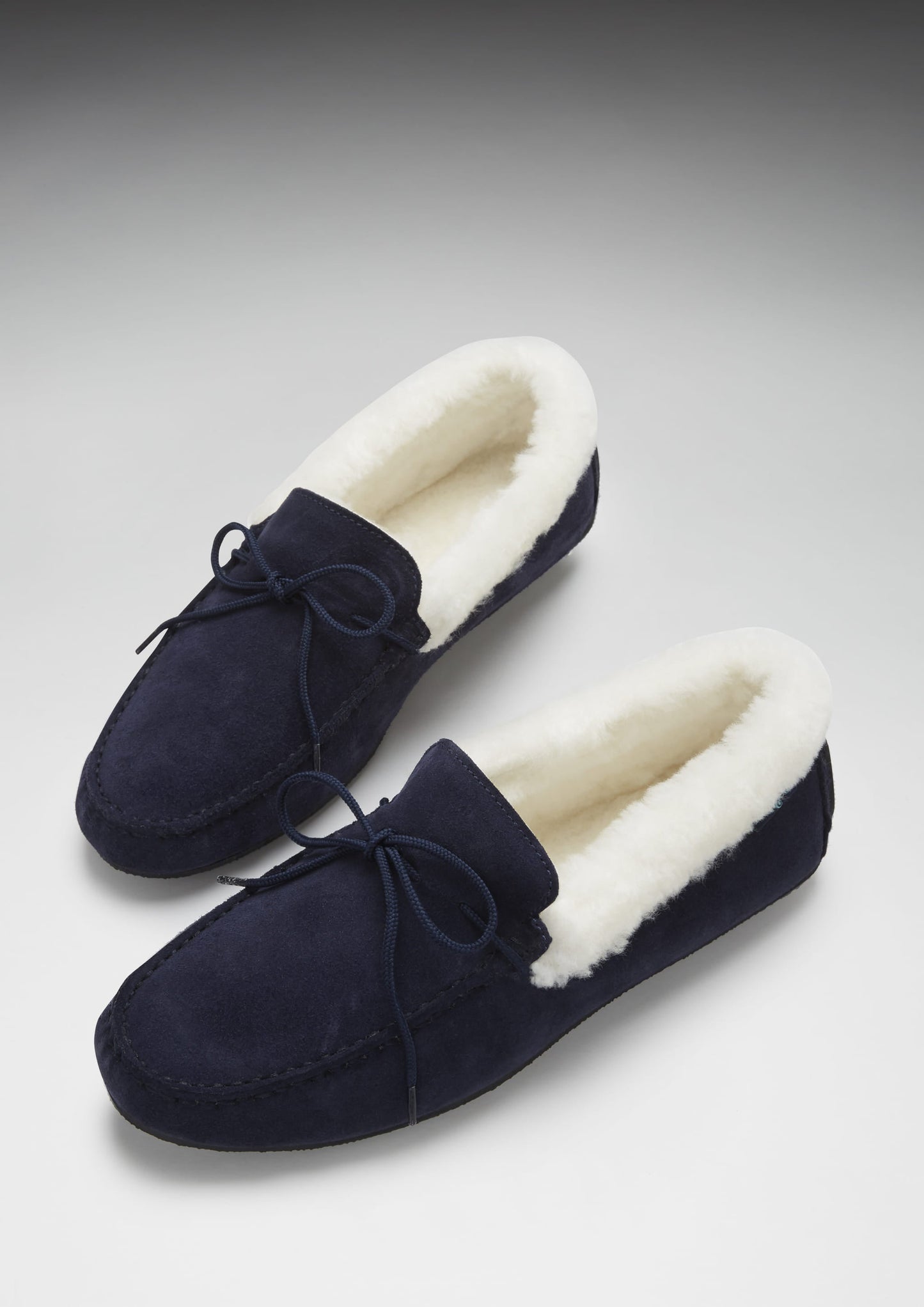 Navy blue slippers with white fur lining on a light gray background