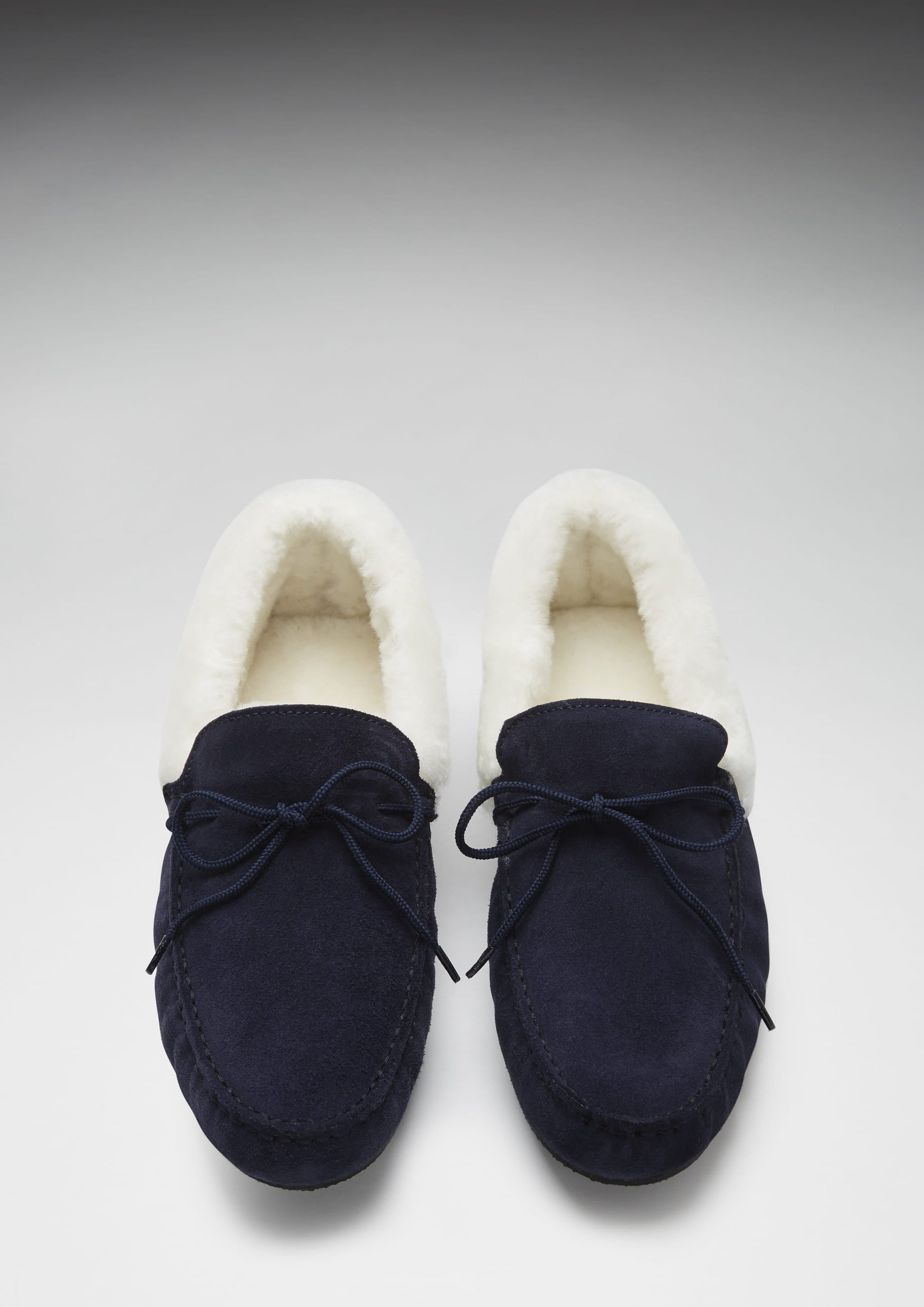 Pair of navy blue moccasin slippers with white fur lining on a light gray background
