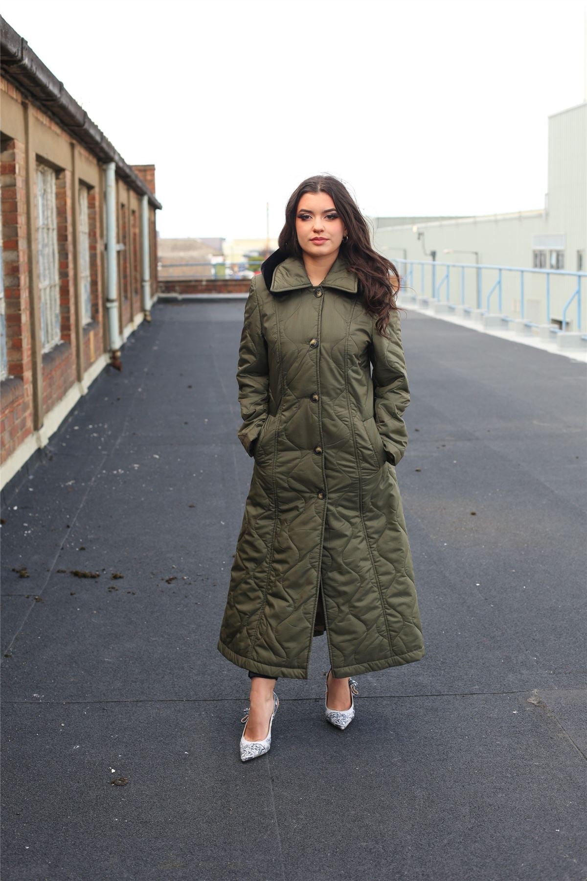 Woman wearing a long green coat on a rooftop.