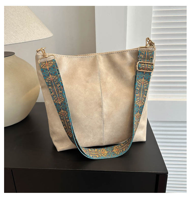 Beige handbag with a decorative blue strap on a dark surface