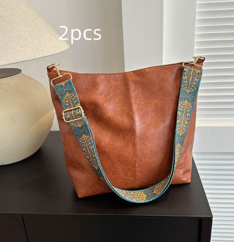 Brown leather handbag with decorative strap on a dark surface
